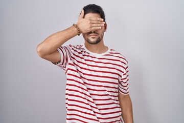 Fototapeta premium Hispanic man with long hair standing over isolated background covering eyes with hand, looking serious and sad. sightless, hiding and rejection concept