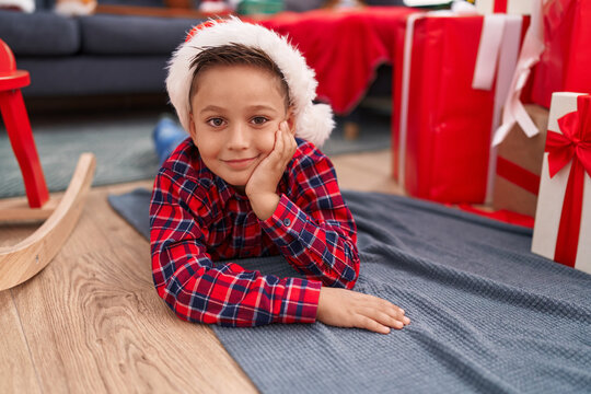Adorable hispanic boy smiling confident lying on floor by christmas gifts at home