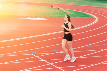 A female coach with dark hair stands on the red running track of the stadium