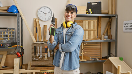 Young hispanic man carpenter wearing glasses and headphones holding drill at carpentry