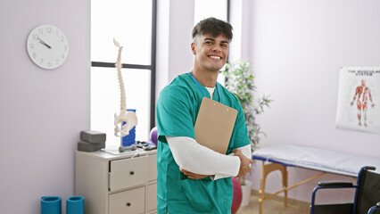 Confident young hispanic man, a beaming physiotherapist, proudly displays his rehabilitation...