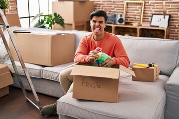 Hispanic man moving to a new home unpacking sticking tongue out happy with funny expression.