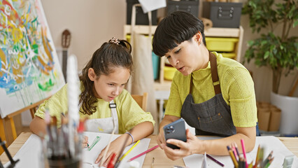 Teacher and student, two painters at heart, bonding over art lesson in studio, joyfully drawing and texting in notebook using smartphone
