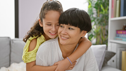 Confident mother and daughter sharing a joyful hug, smiling heartily while sitting on the living room sofa at home â€“ a beautiful expression of family love and happiness