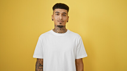 Cool, tattooed young latin man with a serious expression standing alone, casually relaxed against a...