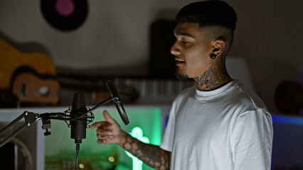 Serious young latin man, a tattooed musician, firing up the night in a music studio, singing his...