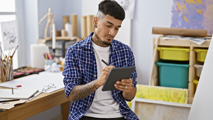 Relaxed young latin man, a tattooed artist, seriously immersed in drawing a portrait on his...