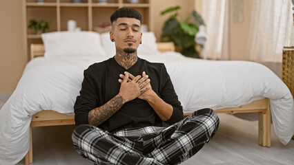 Confident young latin man balancing his morning - posing yoga exercise on bedroom floor, calmly...