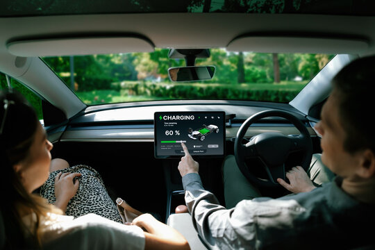 Electric car driver checks battery charging status, range and charging limit on app screen in the car. Smart technology device show EV car recharging data of electric storage in car battery innards. - Powered by Adobe