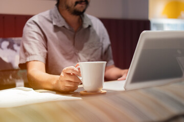 A happy businessman is sitting in a cafe, drinking coffee and watching a webinar on the laptop.
