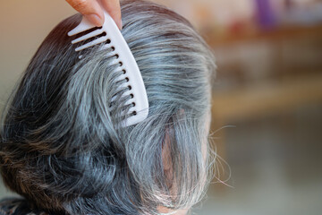 Middle age grey-haired woman on back view combing hair standing at home.