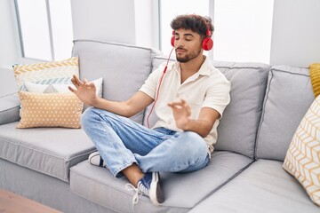Young arab man doing yoga exercise sitting on sofa at home