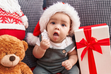 Adorable hispanic toddler sitting on sofa wearing christmas hat at home