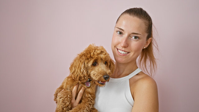 Young caucasian woman with dog smiling hugging over isolated pink background