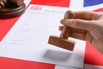 Immigration to United Kingdom. Woman stamping visa application form on flag, closeup