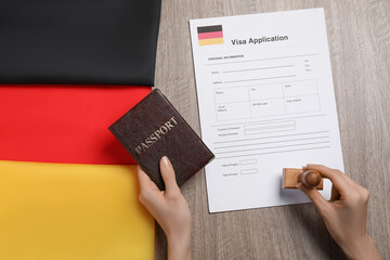 Immigration to Germany. Woman with passport stamping visa application form at wooden table, top view