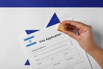 Immigration to Israel. Woman stamping visa application form on flag, top view