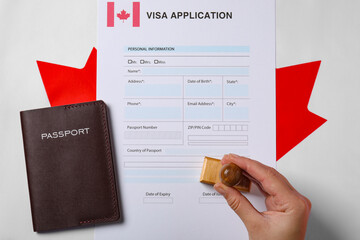 Immigration to Canada. Woman stamping visa application form on flag, top view