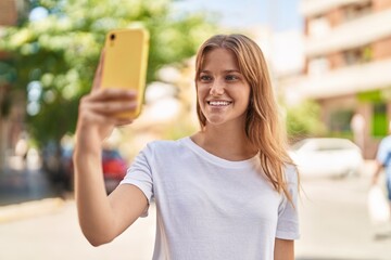 Young blonde girl smiling confident making selfie by the smartphone at street