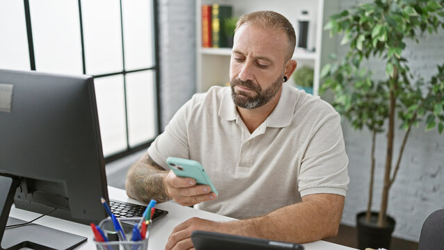 Attractive young business pro acing success as boss man at work - handsome male worker indoors office, multitasking on computer & smartphone - typing text and managing office tasks with elegance