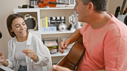 Fototapeta premium Confident hispanic man and woman musicians passionately singing and playing classic guitar at a lively music studio indoors