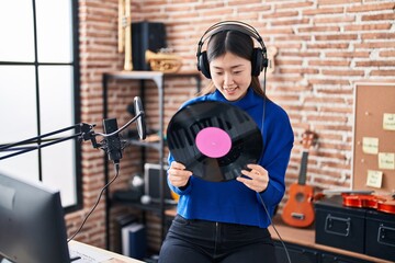 Chinese woman artist smiling confident holding vinyl disc at music studio
