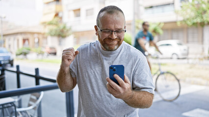 Eureka! cheerful middle-aged caucasian man with beard, firstly celebrating using smartphone on...