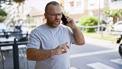 Handsome middle-aged caucasian man standing on sunlit urban street, engrossed in serious phone...