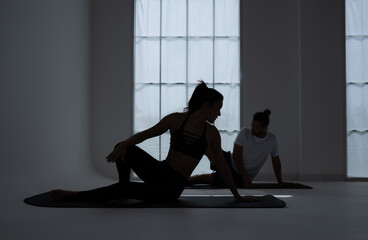 Silhouette of a young couple practicing yoga in the room. - obrazy, fototapety, plakaty