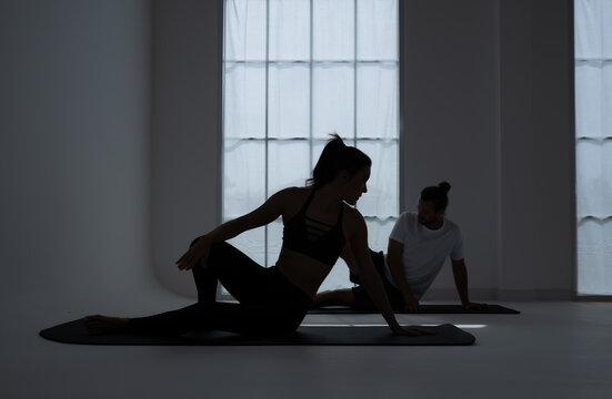 Silhouette of a young couple practicing yoga in the room.