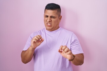 Young hispanic man standing over pink background disgusted expression, displeased and fearful doing disgust face because aversion reaction.