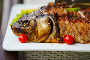 Head of baked fish on a platter with cherry tomatoes. 