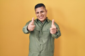 Hispanic young man standing over yellow background pointing fingers to camera with happy and funny face. good energy and vibes.