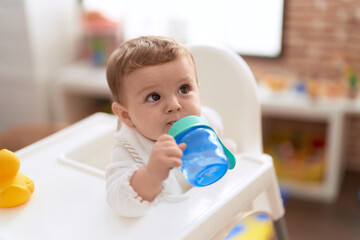 Adorable toddler sitting on baby highchair drinking water at kindergarten