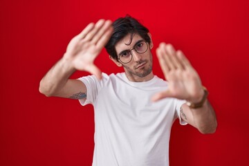 Young hispanic man standing over red background doing frame using hands palms and fingers, camera perspective