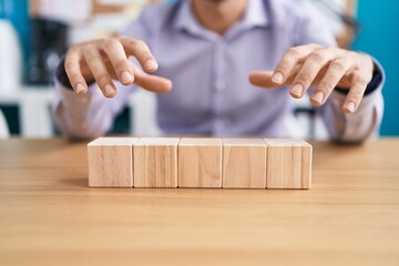 Young hispanic man business worker sitting on table with wooden cubes at office