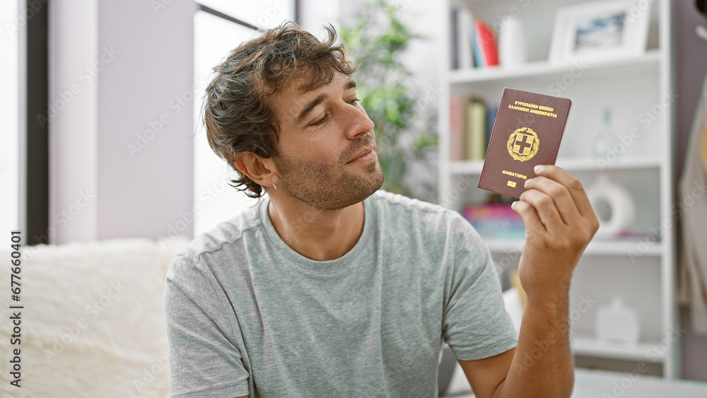 Canvas Prints Delighted young man, a beaming passport holder passes the day in his cozy home, joyously sitting on the sofa embracing his greece heritage.