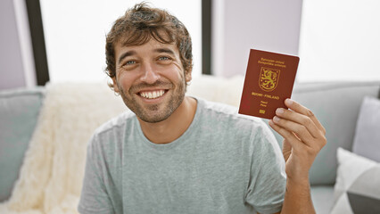 Smiling young man, confidently holding finland passport, chilling at home on the sofa, ready to...