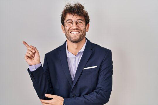 Hispanic business man wearing glasses with a big smile on face, pointing with hand and finger to the side looking at the camera.