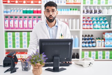 Hispanic man with beard working at pharmacy drugstore afraid and shocked with surprise expression,...