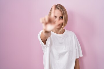 Young caucasian woman standing over pink background pointing with finger up and angry expression, showing no gesture