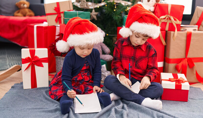 Fototapeta na wymiar Adorable boy and girl drawing on notebook celebrating christmas at home