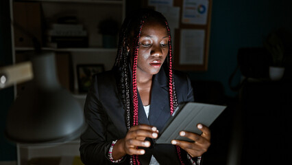 Focused african american woman worker at office, monitors aglow, braids and dark jacket on, nimble...