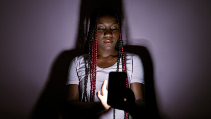 Serious african american woman engrossed in nightly digital communication, using smartphone over...