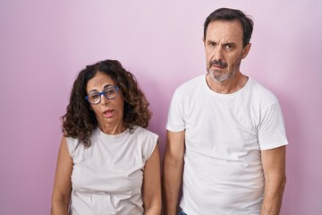Middle age hispanic couple together over pink background looking sleepy and tired, exhausted for fatigue and hangover, lazy eyes in the morning.