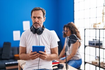 Middle age hispanic man at music studio using tablet skeptic and nervous, frowning upset because of problem. negative person.