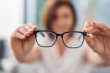 Middle age woman holding glasses sitting on sofa at home