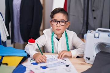 Young hispanic kid at tailor room thinking attitude and sober expression looking self confident