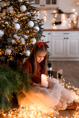 Cheerful small girl indoors at home at Christmas, holding candle - 677667628