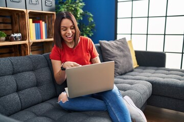 Young hispanic woman using laptop at home smiling happy pointing with hand and finger